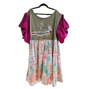 Puede incluir: Vestido verde oliva con mangas rosas con volantes y una falda floral. La parte superior presenta un gráfico de un esqueleto y un perro dálmata. El texto en el vestido dice "This stuff goes right through me."