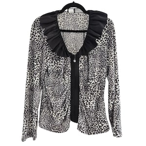 May include: A long-sleeved leopard print jacket with a black ruffled collar and a black zipper closure. The jacket is hanging on a black hanger against a white background. The jacket has a black and white animal print.