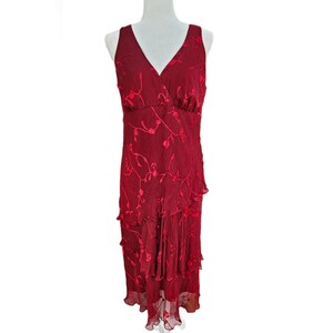 May include: A sleeveless midi dress in deep red featuring a V-neckline and a layered, ruffled skirt. The fabric is adorned with a tonal, embroidered floral vine pattern that extends across the bodice and down to the hemline of the garment.