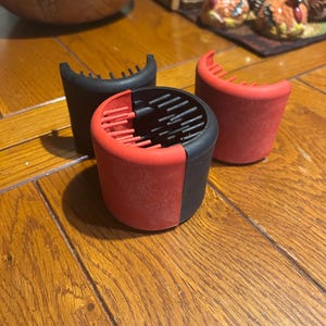May include: Three black and red silicone kitchen gadgets with a comb-like design. The gadgets are on a wooden table.