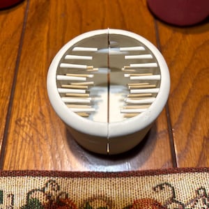 May include: White plastic container with a divided top. The top has a series of small, white, vertical dividers.