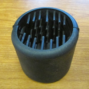May include: A black rubber mold with a circular opening and a grid of small holes inside. The mold is designed for creating objects with a textured surface.