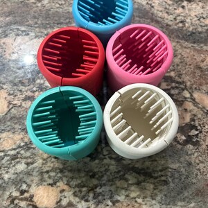 May include: Five silicone hair curlers in different colors: blue, red, pink, teal, and white. Each curler has a textured surface with ridges.