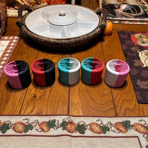 May include: Five round hair rollers in different colors. The rollers are split in half, with one half black and the other half a different color. The colors are pink, red, teal, red, and pink.