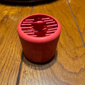 May include: A red silicone kitchen tool with a ridged surface. The tool is designed for cleaning vegetables.