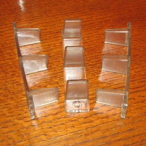 May include: Nine clear plastic corner protectors for furniture. The protectors are shaped like a right triangle with a small hole in the center of the hypotenuse.