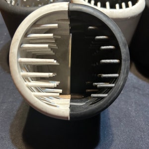 May include: A close-up of a black and white 3D printed object with a grid pattern. The object is split in half, with one side black and the other white.