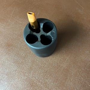 May include: A black pencil holder with four compartments, one of which holds a yellow and gold pencil.