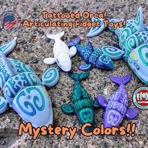 May include: Five colorful articulated orca fidget toys. Each orca has a different color scheme with green, blue, and purple swirls. The text "Tattooed Orca! Articulating Fidget Toys! Mystery Colors!!" is printed on the image.