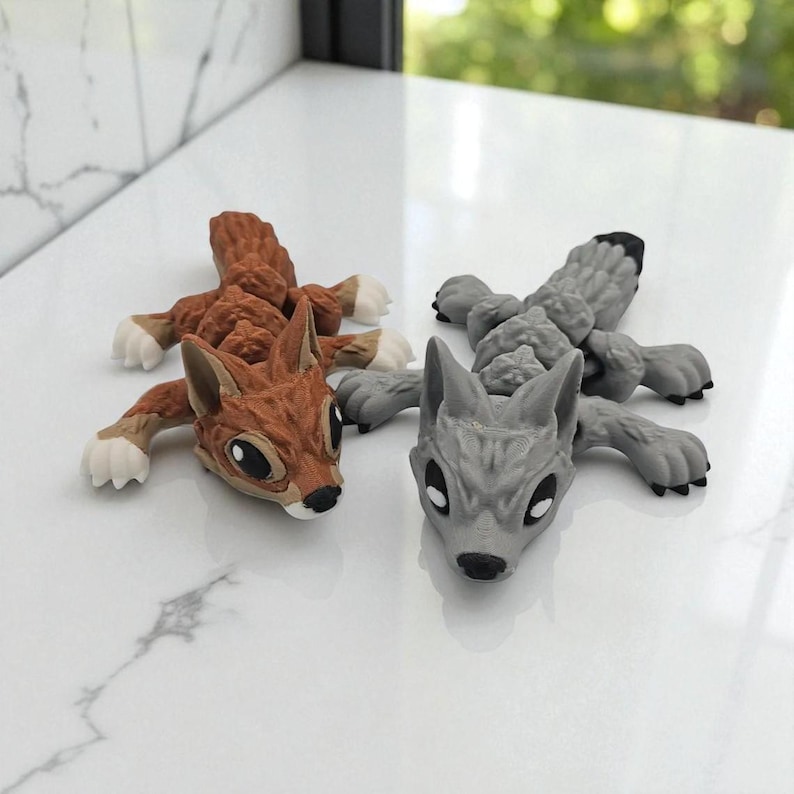 Peut inclure: Deux figurines d'animaux : un &eacute;cureuil brun et un loup gris. L'&eacute;cureuil a des pattes blanches et un ventre blanc. Le loup a une pointe noire sur sa queue. Les deux sont allong&eacute;s, les pattes tendues.
