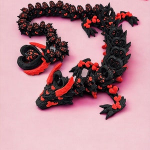 Op de afbeelding: Een zwart en rood 3D-geprint drakenbeeld met een hartvormig ontwerp. De draak is opgerold in een cirkel met zijn staart in zijn bek.