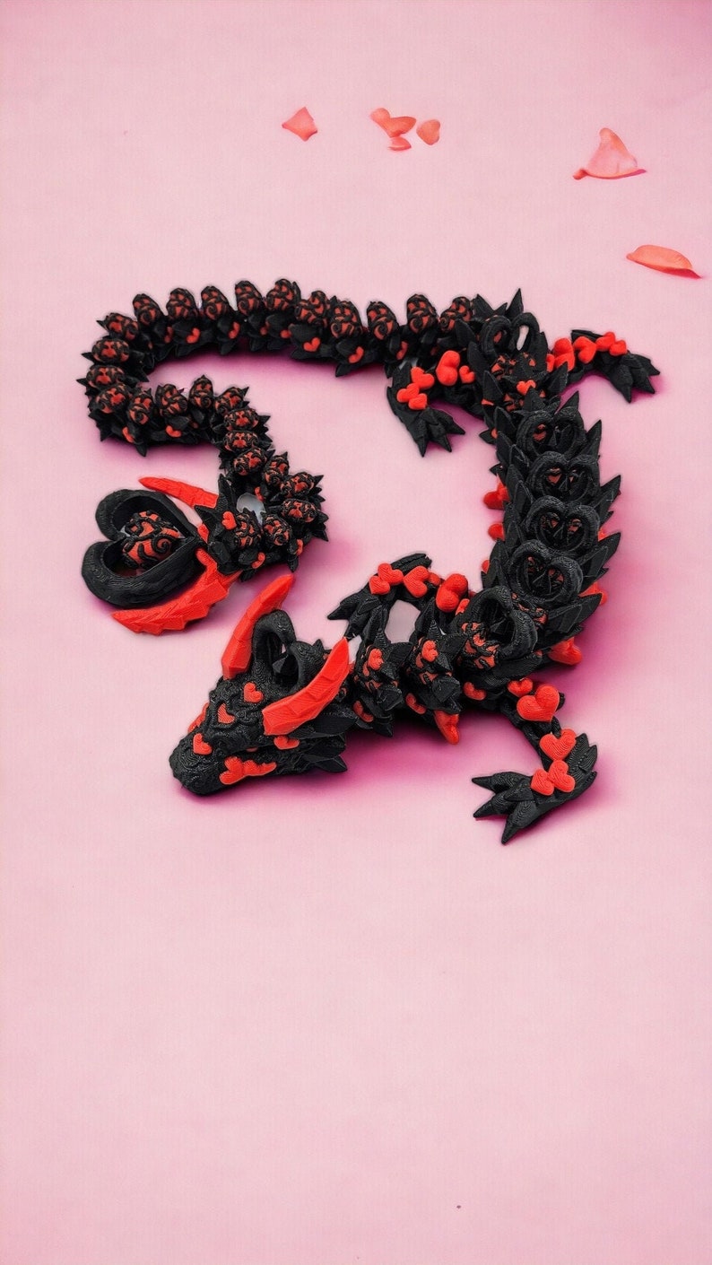 Op de afbeelding: Een zwart en rood 3D-geprint drakenbeeld met een hartvormig ontwerp. De draak is opgerold in een cirkel met zijn staart in zijn bek.