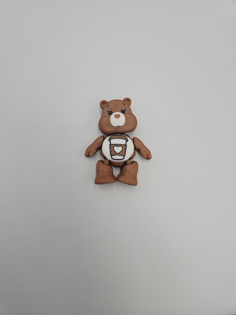 May include: A brown bear figurine with a white belly featuring a coffee cup design. The bear has a smiling face and is standing upright. The figurine is made of a smooth material and is set against a plain white background.