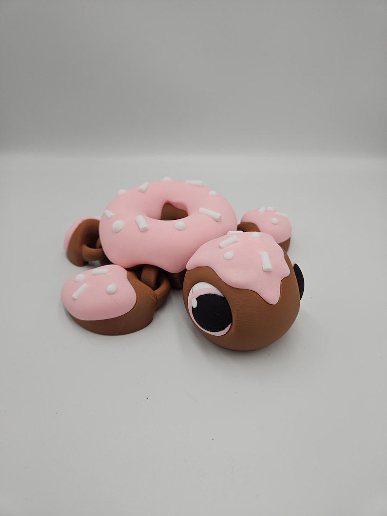 Pode incluir: Uma escultura extravagante em forma de donut, com cobertura rosa e granulado branco. A escultura tem uma base marrom e &eacute; acompanhada por pe&ccedil;as menores semelhantes, criando um design l&uacute;dico com tema de comida. O donut tem um buraco no centro.