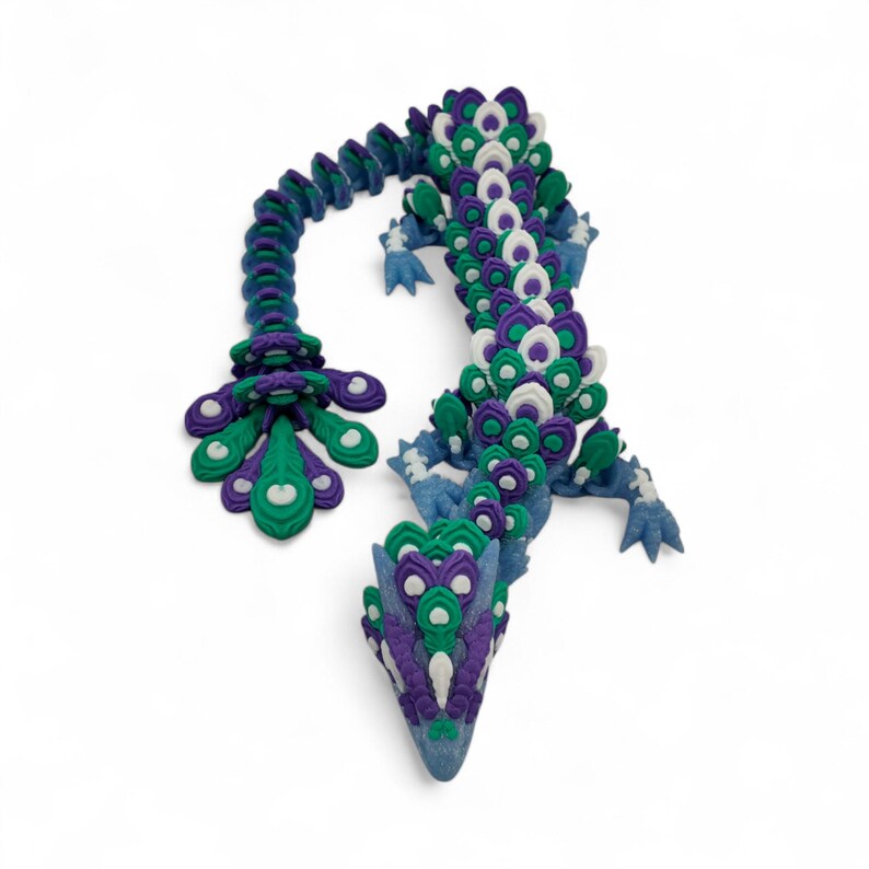 May include: A handcrafted, whimsical dragon sculpture in shades of blue, green, purple, and white. The dragon's body is intricately detailed with layered, petal-like shapes, and it has a long, curved tail. The sculpture is set against a white background.