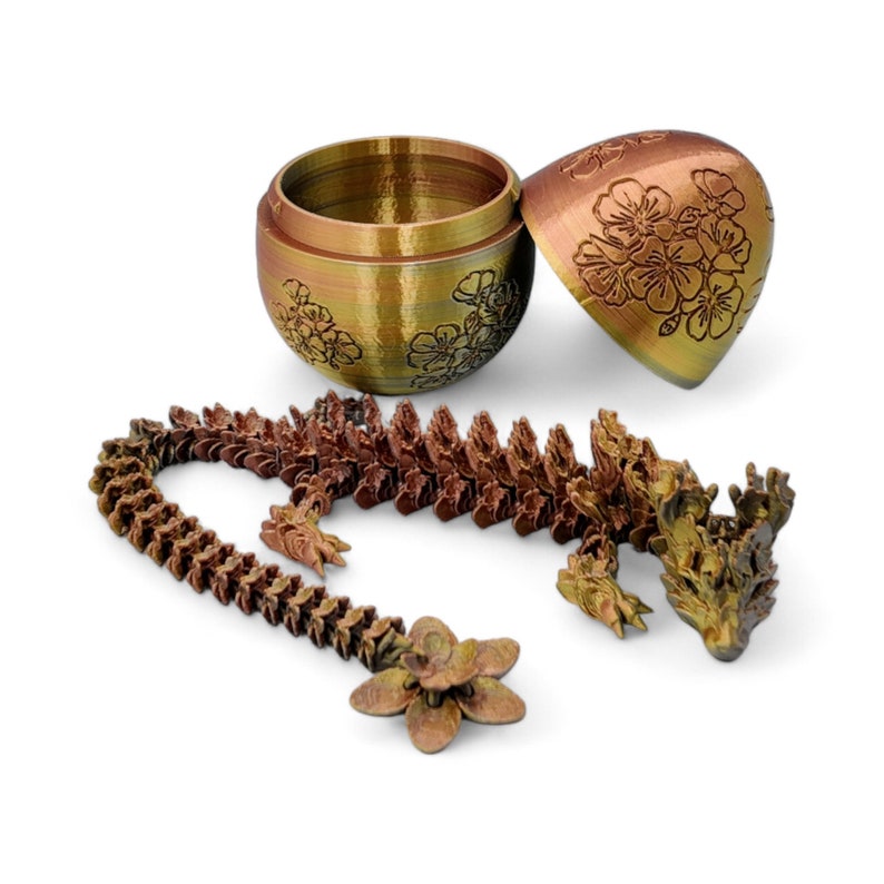 Pu&ograve; includere: Una statuetta di drago color oro e rame con un design floreale. Il drago &egrave; arrotolato su se stesso con la testa appoggiata sulla coda. Il drago fa parte di un set che include un contenitore a forma di uovo abbinato.