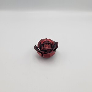 May include: A single, deep red rose with dark edges, set against a white background. The rose is in full bloom, showcasing detailed petals and a textured appearance. The overall aesthetic is elegant and simple.