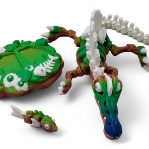 May include: A 3D printed green and white skeletal dinosaur with a blue snout. The dinosaur is posed on a green and brown base with a fish bone design. The dinosaur is part of a tabletop game.
