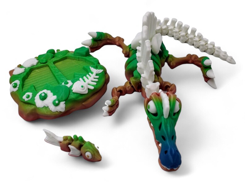 May include: A 3D printed green and white skeletal dinosaur with a blue snout. The dinosaur is posed on a green and brown base with a fish bone design. The dinosaur is part of a tabletop game.