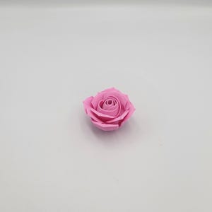 May include: A single, light pink rose with tightly packed petals. The artificial flower is centered on a white background, showcasing its delicate form and color. The rose's design mimics a natural bloom.