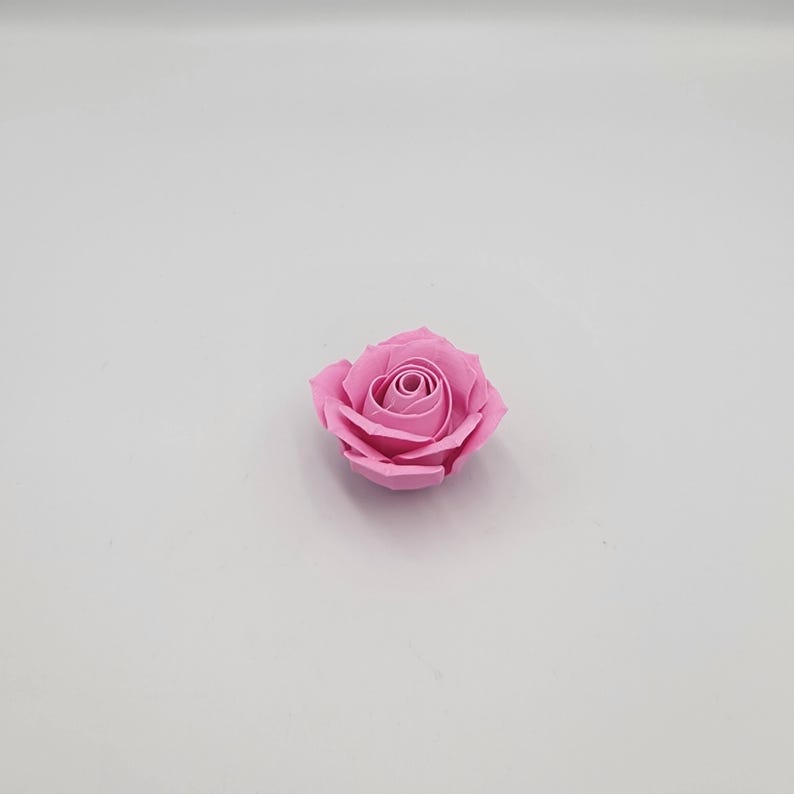 May include: A single, light pink rose with tightly packed petals. The artificial flower is centered on a white background, showcasing its delicate form and color. The rose's design mimics a natural bloom.