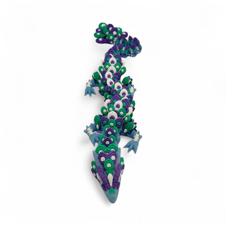 May include: A handcrafted, decorative lizard sculpture in shades of blue, green, purple, and white. The lizard's body is made of layered, circular shapes, with a detailed tail and four small feet. The sculpture is set against a white background.
