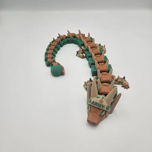 Pode incluir: Um brinquedo de drag&atilde;o segmentado em tons de verde e castanho. O corpo do drag&atilde;o &eacute; feito de blocos retangulares, com uma cabe&ccedil;a e cauda arredondadas. A cabe&ccedil;a tem a palavra "ARMY" impressa.