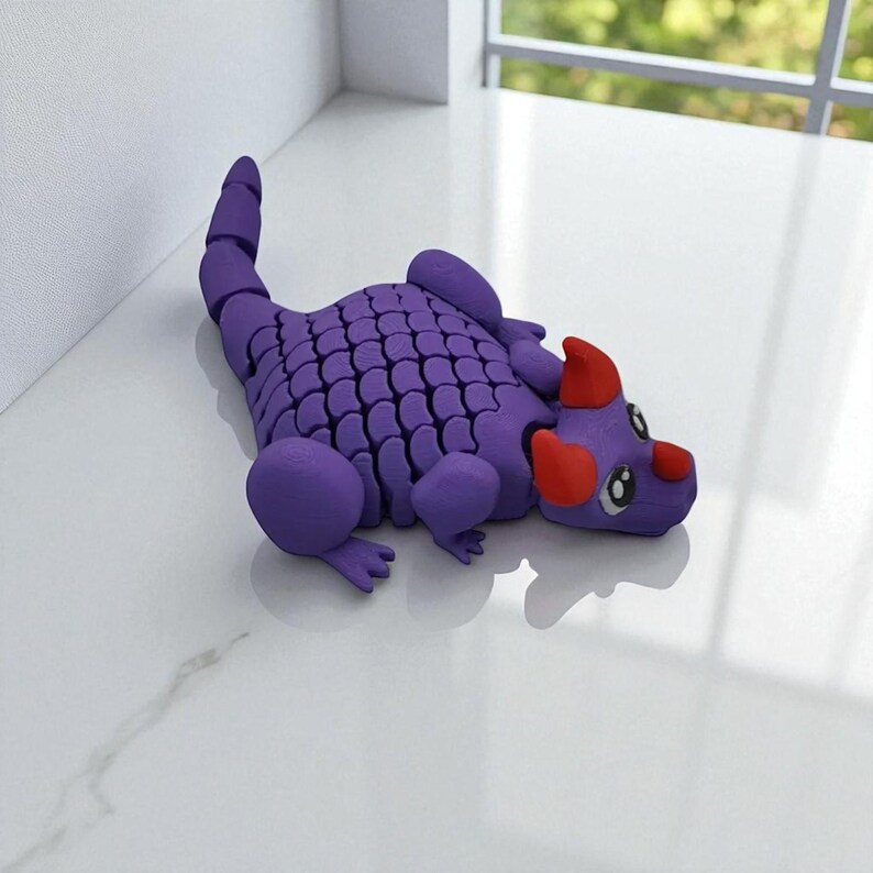 Puede incluir: Una figura de drag&oacute;n morado con un cuerpo segmentado y una espalda escamada. El drag&oacute;n tiene cuernos rojos y detalles en forma de coraz&oacute;n cerca de los ojos. La figura est&aacute; sobre una superficie blanca.