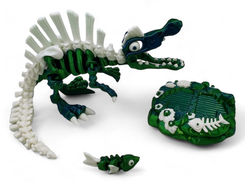May include: A green and white plastic dinosaur skeleton toy with a white spine and a green body. The dinosaur is standing on a green and white base with a fish bone design. A smaller green and white fish skeleton toy is in the foreground.