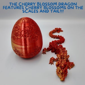 Pu&ograve; includere: Un drago stampato in 3D rosso e oro con dettagli di fiori di ciliegio. Il drago &egrave; rannicchiato in una posizione di riposo. Il drago &egrave; accanto a un uovo rosso con dettagli di fiori di ciliegio.