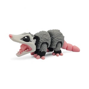 May include: A gray and white opossum figurine with a pink nose, mouth, and tail. The figurine has black paws and ears. The opossum's mouth is open, revealing pink teeth and tongue. The figurine is on a white background.
