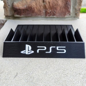 May include: Black plastic game case with slots for storing video game discs. The case has a PlayStation logo and the text "PS5" printed on the front.