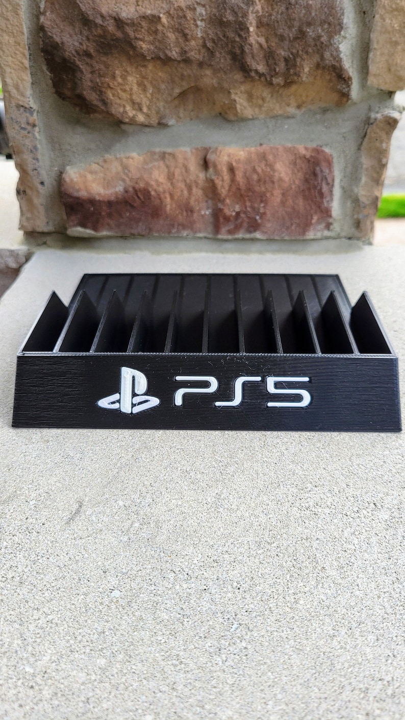 May include: Black plastic game case with slots for storing video game discs. The case has a PlayStation logo and the text "PS5" printed on the front.