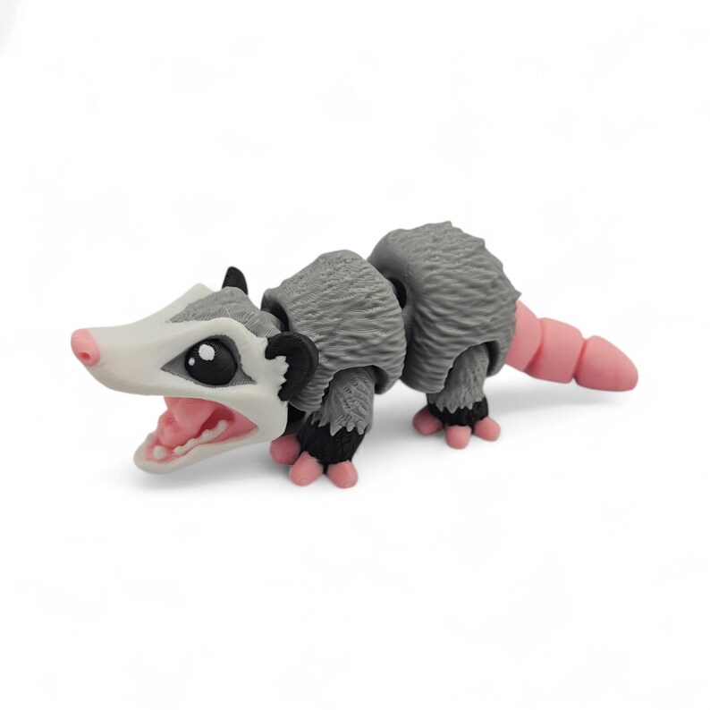 May include: A gray and white opossum figurine with a pink tail, nose, and mouth. The opossum has black ears and feet. The figurine is posed with its mouth open, revealing pink details.
