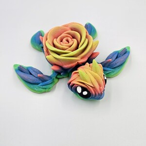 May include: A rainbow-colored turtle figurine with a rose for a shell. The turtle has large, black eyes and a detailed, textured surface.