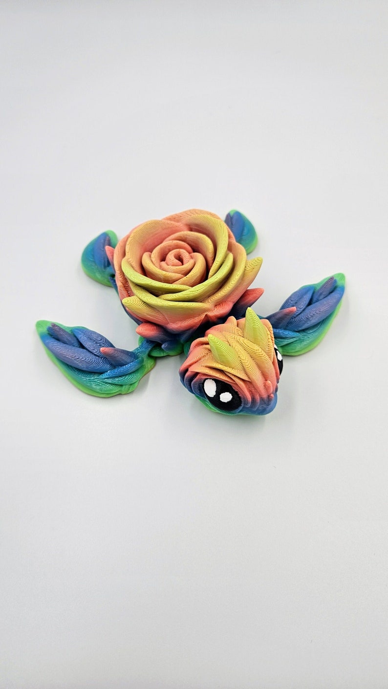 May include: A rainbow-colored turtle figurine with a rose for a shell. The turtle has large, black eyes and a detailed, textured surface.