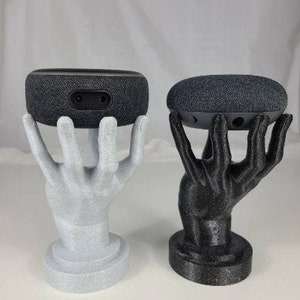 Op de afbeelding: Twee 3D-geprinte handen die een zwarte en een grijze slimme speaker vasthouden. De handen zijn in lichtgrijs en zwart geverfd.