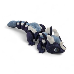 May include: A dark blue dragon figurine with light blue and white accents. The dragon has a segmented body, snowflake details, and large, expressive eyes. The figurine is a fantasy-themed collectible.
