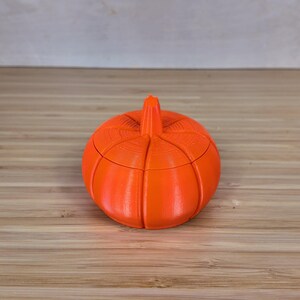 May include: A bright orange pumpkin-shaped container with a lid. The container is made of plastic and has a smooth, rounded surface.