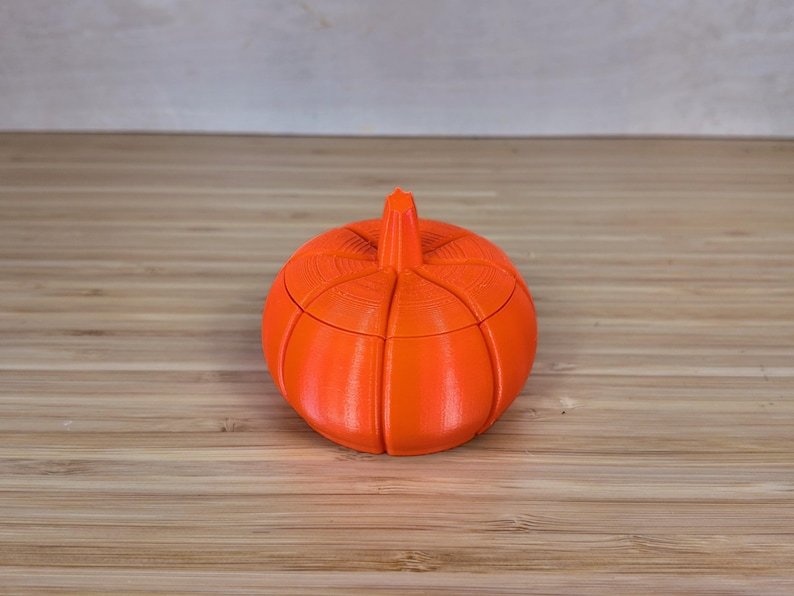 May include: A bright orange pumpkin-shaped container with a lid. The container is made of plastic and has a smooth, rounded surface.