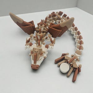 以下が含まれることがあります： 茶色、ベージュ、白の色合いの手作りのドラゴン彫刻。ドラゴンは、詳細な翼、セグメント化された体、複雑なディテールを備えており、ユニークな芸術的スタイルを示しています。彫刻は装飾品です。