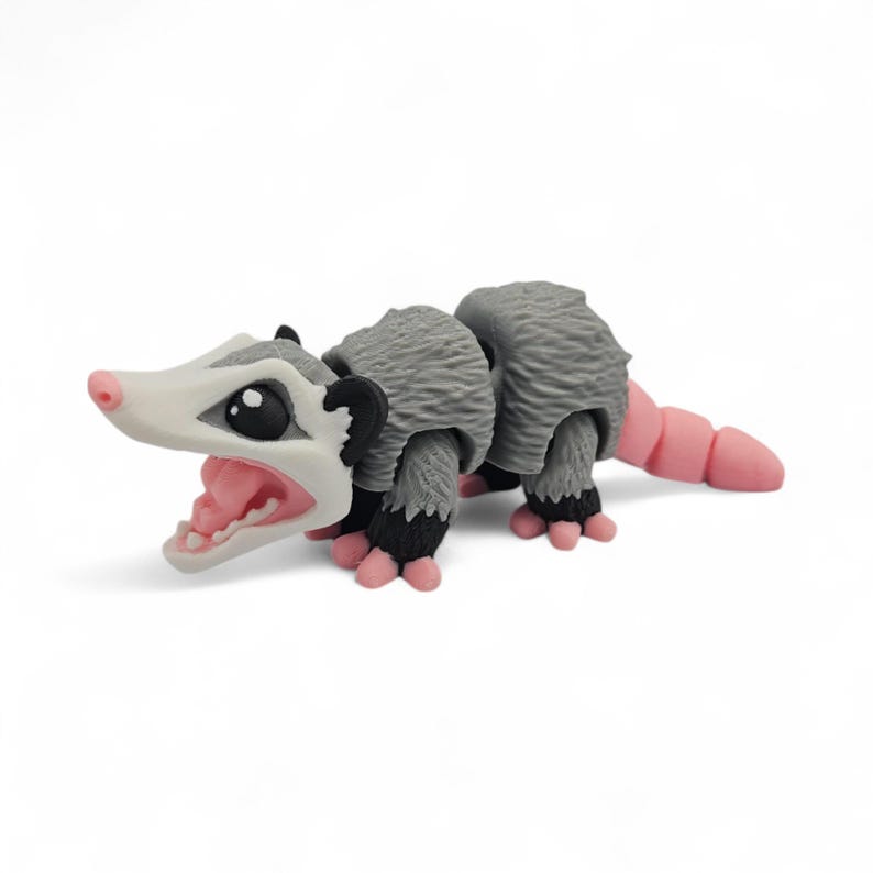 May include: A gray and white opossum figurine with a pink nose, tail, and feet. The opossum has a wide open mouth with pink gums and teeth. The figurine has black eyes and ears.