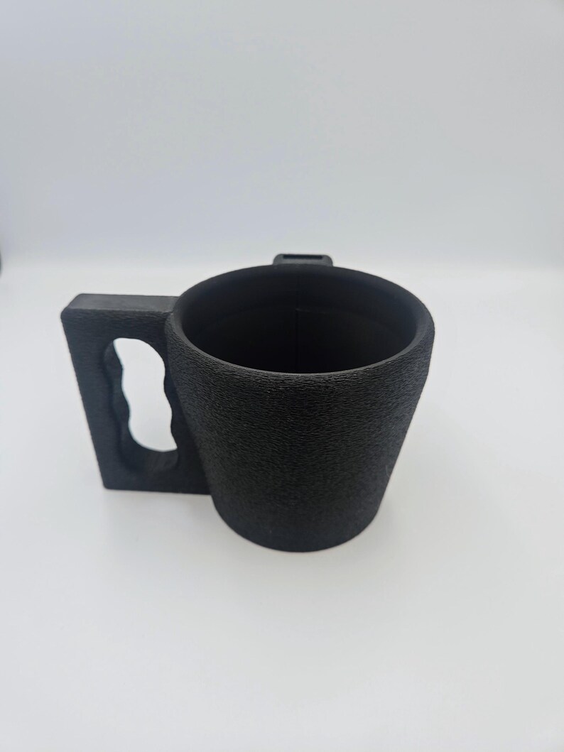 Pu&ograve; includere: Una tazza nera con una superficie strutturata e un'ampia maniglia rettangolare. Il manico ha un ritaglio per l'impugnatura. La tazza &egrave; cilindrica con una parte superiore leggermente svasata.