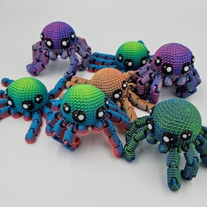 Op de afbeelding: Een set van zes kleurrijke gehaakte spinnen speelgoed. Elke spin heeft een andere kleurencombinatie van blauw, groen, paars en oranje. De spinnen hebben grote, ronde ogen en zijn gemaakt van een getextureerd garen.
