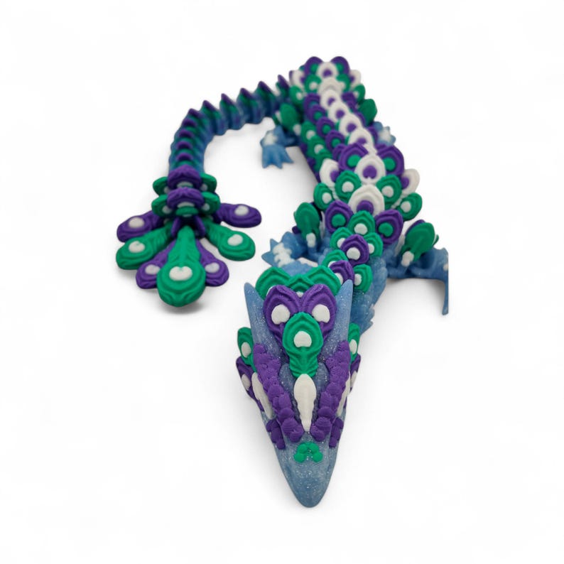 May include: A whimsical, handcrafted dragon sculpture in shades of blue, purple, green, and white. The dragon's body is adorned with intricate, feather-like details, and the head is pointed. The sculpture is set against a white background.