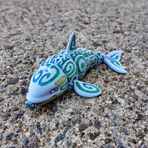 May include: A blue and green toy shark with a swirling pattern. The shark has a toothy grin and is made of plastic.