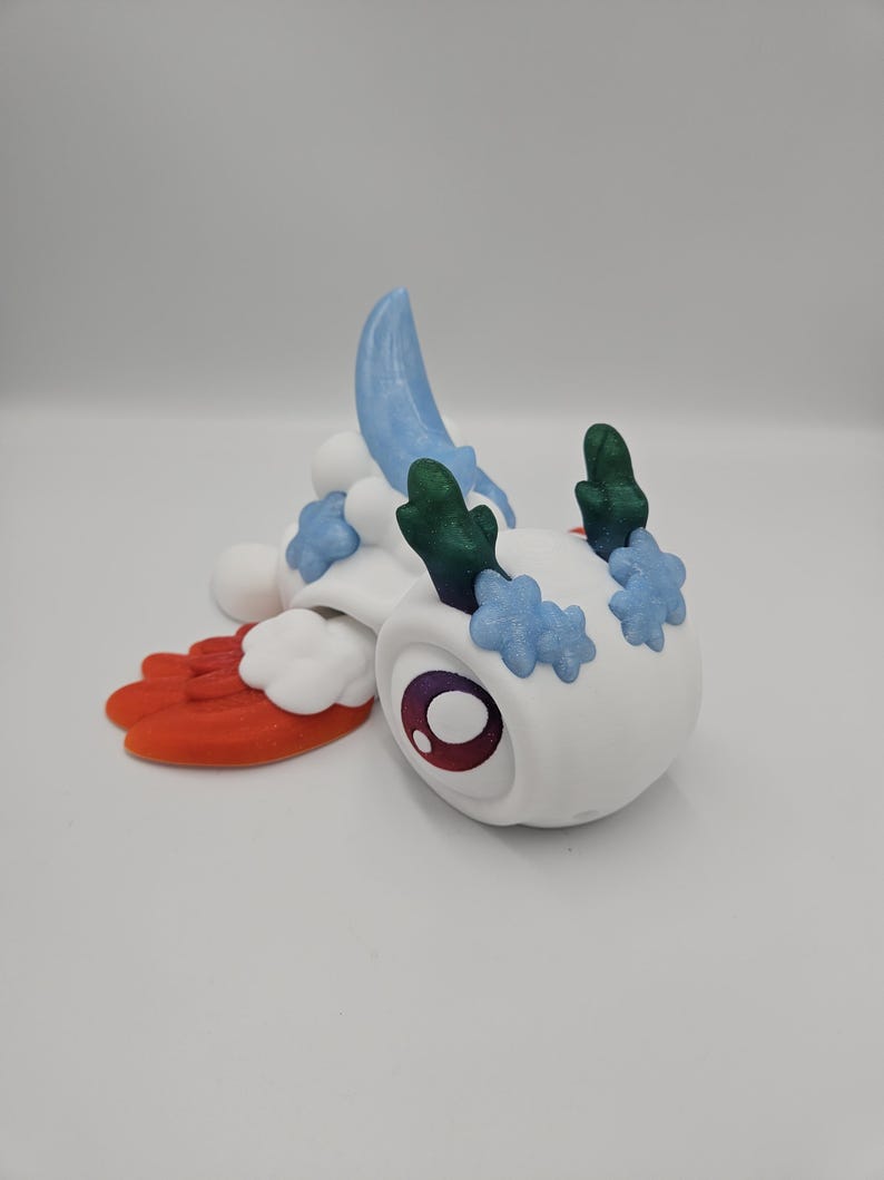 Pode incluir: Uma figura de criatura branca e caprichosa com um olho grande e redondo e detalhes coloridos. Apresenta detalhes azuis, verdes e vermelhos, com um corpo semelhante a uma nuvem e uma asa estilizada. O design &eacute; l&uacute;dico e imaginativo.
