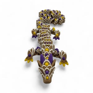 May include: A brown dragon figurine with white, yellow, and purple accents. The dragon is decorated with intricate patterns and details, and is lying on a white surface. The dragon's head is facing the viewer.