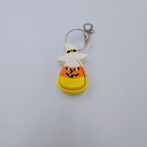 May include: A white and orange candy corn keychain with a black witch hat and a smiling jack-o'-lantern face.