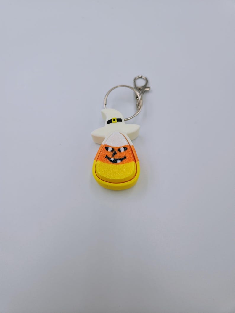 May include: A white and orange candy corn keychain with a black witch hat and a smiling jack-o'-lantern face.